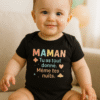 Bébé d’environ 12 mois assis sur un canapé, portant un body noir AnCa Bébé avec le message « MAMAN, tu as tout donné. Même tes nuits. », lumière naturelle douce