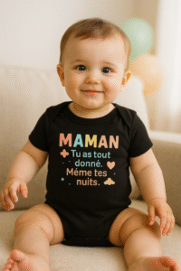 Bébé d’environ 12 mois assis sur un canapé, portant un body noir AnCa Bébé avec le message « MAMAN, tu as tout donné. Même tes nuits. », lumière naturelle douce