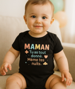 Bébé d’environ 12 mois assis sur un canapé, portant un body noir AnCa Bébé avec le message « MAMAN, tu as tout donné. Même tes nuits. », lumière naturelle douce